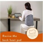 Back view of woman working on laptop at desk with heat pad on her back, promoting comfortable ergonomic office setup.